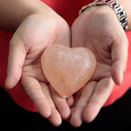 Hands holding a heart-shaped Himalayan pink salt deodorant stone.