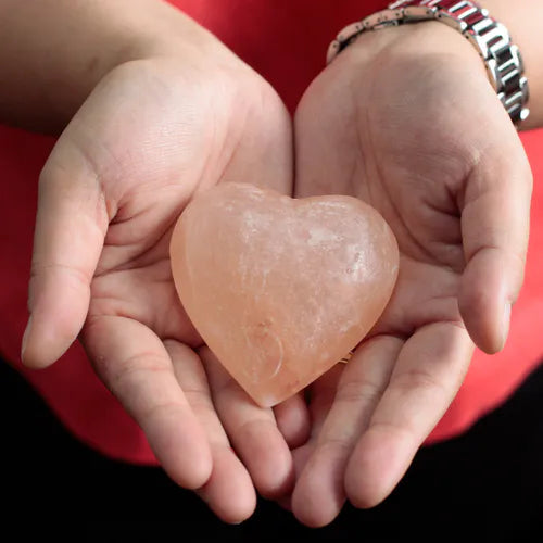 Hands holding a heart-shaped Himalayan pink salt deodorant stone.