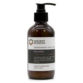 Brown plastic pump bottle of Ancient Wisdom Aromatherapy Hand + Body Lotion. The label is white with black and lavender accents, featuring the text "Relaxing" with clary sage and lavender. The lotion is described as 100% pure and natural oil-based, with no artificial fragrances, enriched with hydrating sunflower oil and avocado oil. The bottle contains 250ml (8.45oz) and is made in England.