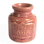 Close-up of a rose glazed ceramic oil burner with raised text on the front reading “LOVE HOME SWEET HOME.” The surface has a glossy finish and subtle crackle effect under the glaze.