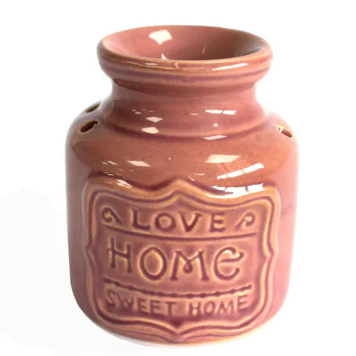 Close-up of a rose glazed ceramic oil burner with raised text on the front reading “LOVE HOME SWEET HOME.” The surface has a glossy finish and subtle crackle effect under the glaze.