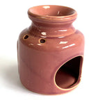 Rear view of a rose glazed ceramic oil burner with glossy finish, showing two round ventilation holes near the neck and a wide arched opening at the base for candle placement.