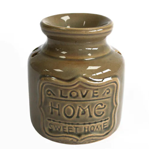 Close-up of a brown glazed ceramic oil burner with embossed text reading “LOVE HOME SWEET HOME” on the front. The object has a glossy finish, circular ventilation holes, and a recessed opening below.