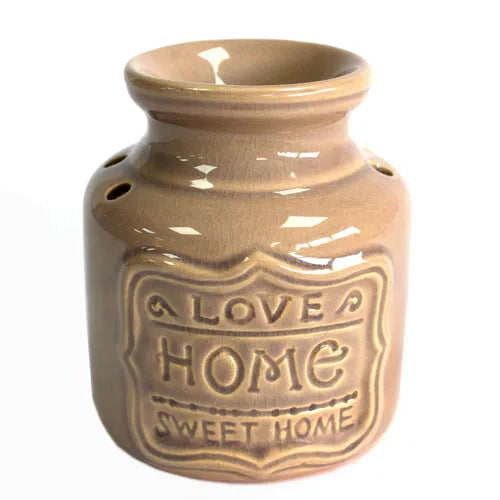 Close-up of a beige ceramic oil burner with a glossy glaze. The front has raised decorative text that reads “LOVE HOME SWEET HOME.” The surface shows light crackle patterns under the glaze.