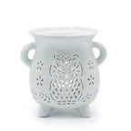 White ceramic oil burner with a rounded, vase-like shape and two side handles. The front is decorated with a detailed cut-out owl design surrounded by small flower-shaped perforations. The burner stands on three short legs, and the top features a wide bowl for holding essential oils or wax melts. Glossy finish adds a polished appearance.
