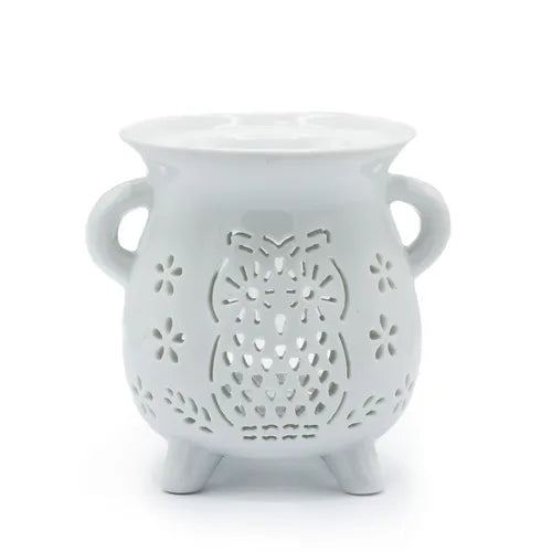 White ceramic oil burner with a rounded, vase-like shape and two side handles. The front is decorated with a detailed cut-out owl design surrounded by small flower-shaped perforations. The burner stands on three short legs, and the top features a wide bowl for holding essential oils or wax melts. Glossy finish adds a polished appearance.