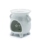 Angled view of a white ceramic oil burner with a glossy finish, rounded body, and two side handles. The front shows a large cut-out opening where a tealight candle can be placed, and floral-shaped perforations are visible on the inner back panel. The oil burner stands on three short legs, with a shallow bowl at the top for oils or wax melts.