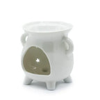 White ceramic oil burner shown from the side angle, featuring two small handles and three supporting legs. A large oval opening at the back provides access for placing a tealight candle inside, while a star-shaped cutout on the opposite wall allows light to shine through. The smooth glossy surface highlights its simple, elegant design.