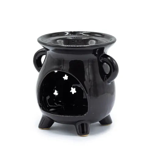 Black ceramic oil burner shaped like a small cauldron, standing on three legs with two side handles. The front has a large cut-out opening with three star-shaped perforations in the back wall, allowing light from a tealight candle to shine through. The glossy surface reflects light, giving it a polished look.