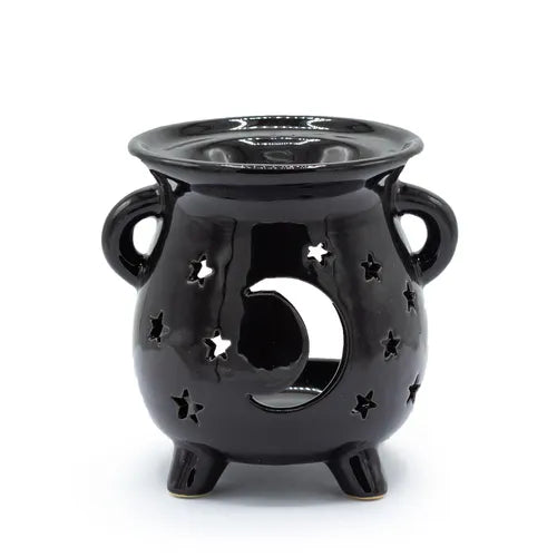 Glossy black ceramic oil burner designed like a cauldron with two side handles and three legs. The front features a large crescent moon cut-out surrounded by multiple star-shaped perforations, creating a celestial theme. The polished surface enhances its decorative appeal while allowing candlelight to project through the cut-outs.