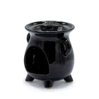 Black ceramic oil burner shaped like a small cauldron with two side handles and three legs. The back view shows a large rounded opening to place a tealight inside. The interior is glossy and smooth, with light able to shine through the cut-out patterns on the opposite side.
