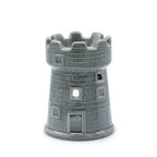Gray ceramic oil burner designed as a medieval-style tower, featuring a crenellated top rim and textured brick-like surface. The piece has several cut-out windows of different square shapes and a small rectangular door opening at the bottom to insert a tealight candle. The glossy glaze enhances the castle-like appearance.