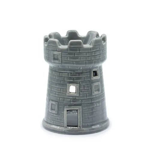 Gray ceramic oil burner designed as a medieval-style tower, featuring a crenellated top rim and textured brick-like surface. The piece has several cut-out windows of different square shapes and a small rectangular door opening at the bottom to insert a tealight candle. The glossy glaze enhances the castle-like appearance.