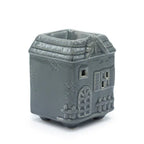 Grey ceramic oil burner shaped like a small house with a pitched roof, decorative details like windows, a door, and textured stone walls.