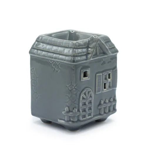 Grey ceramic oil burner shaped like a small house with a pitched roof, decorative details like windows, a door, and textured stone walls.