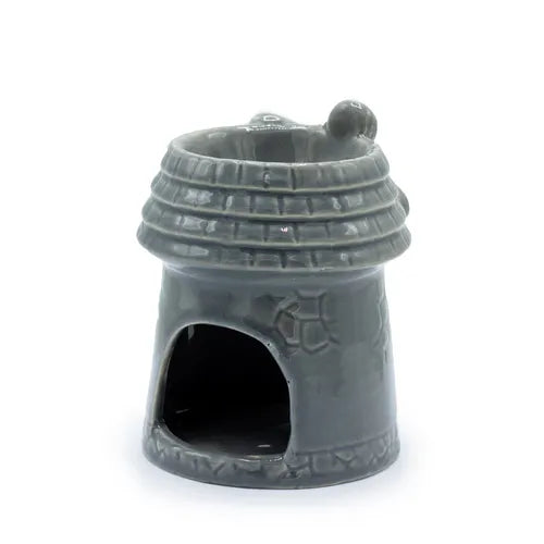 Gray ceramic oil burner in the shape of a windmill tower, shown from the back. The surface is decorated with a brick-like pattern, and there is a wide arched cut-out at the base to place a tealight candle inside. The upper part has a circular bowl opening, with a rounded detail on the side of the roof structure.