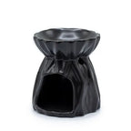 Black ceramic oil burner designed with a draped fabric-like texture, showing a wide open cutout at the base for placing a tealight candle. The top part has a wide bowl for oils or wax melts, while a small circular hole on the side provides ventilation.