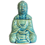 Complete turquoise ceramic oil burner shaped as a seated Buddha figure. The Buddha is shown with a serene facial expression and detailed robe patterns, finished with a glossy crackle glaze. The head serves as a removable lid for the tealight compartment.