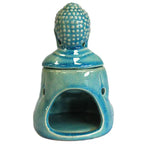 Ceramic oil burner in turquoise blue glaze shaped like a Buddha figure. The back shows an open cavity for placing a tealight candle, with the head of the Buddha forming the removable lid. The surface is glossy with a crackled glaze effect.