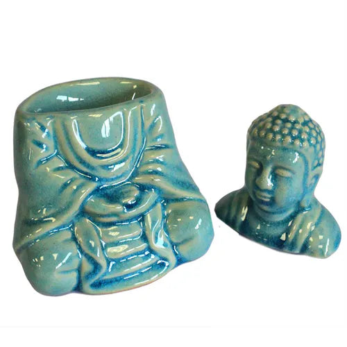 Disassembled turquoise ceramic oil burner shaped like a Buddha. The body, decorated with robe details, has an open cavity for the tealight, while the separate Buddha head piece is designed to sit on top. Both pieces feature glossy crackle glaze.