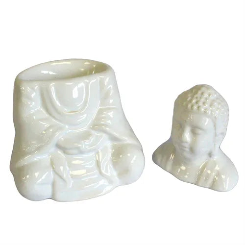 White ceramic oil burner in two separate parts: the hollow base shaped like a seated Buddha body with draped robes, and the detachable Buddha head placed beside it. The glossy surface emphasizes the sculpted folds and facial details.