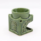 Side view of a green ceramic Buddha oil burner with embossed Buddha face and decorative floral patterns. The top bowl is designed for holding essential oils or wax melts, while the lower hollow section accommodates a tealight candle for fragrance diffusion.