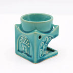 Turquoise ceramic oil burner with a carved Buddha face and floral motifs, featuring a top bowl for essential oils and an open cavity for a tealight candle.