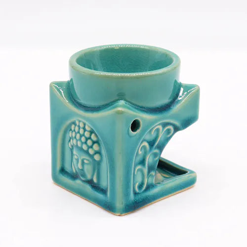 Turquoise ceramic oil burner with a carved Buddha face and floral motifs, featuring a top bowl for essential oils and an open cavity for a tealight candle.