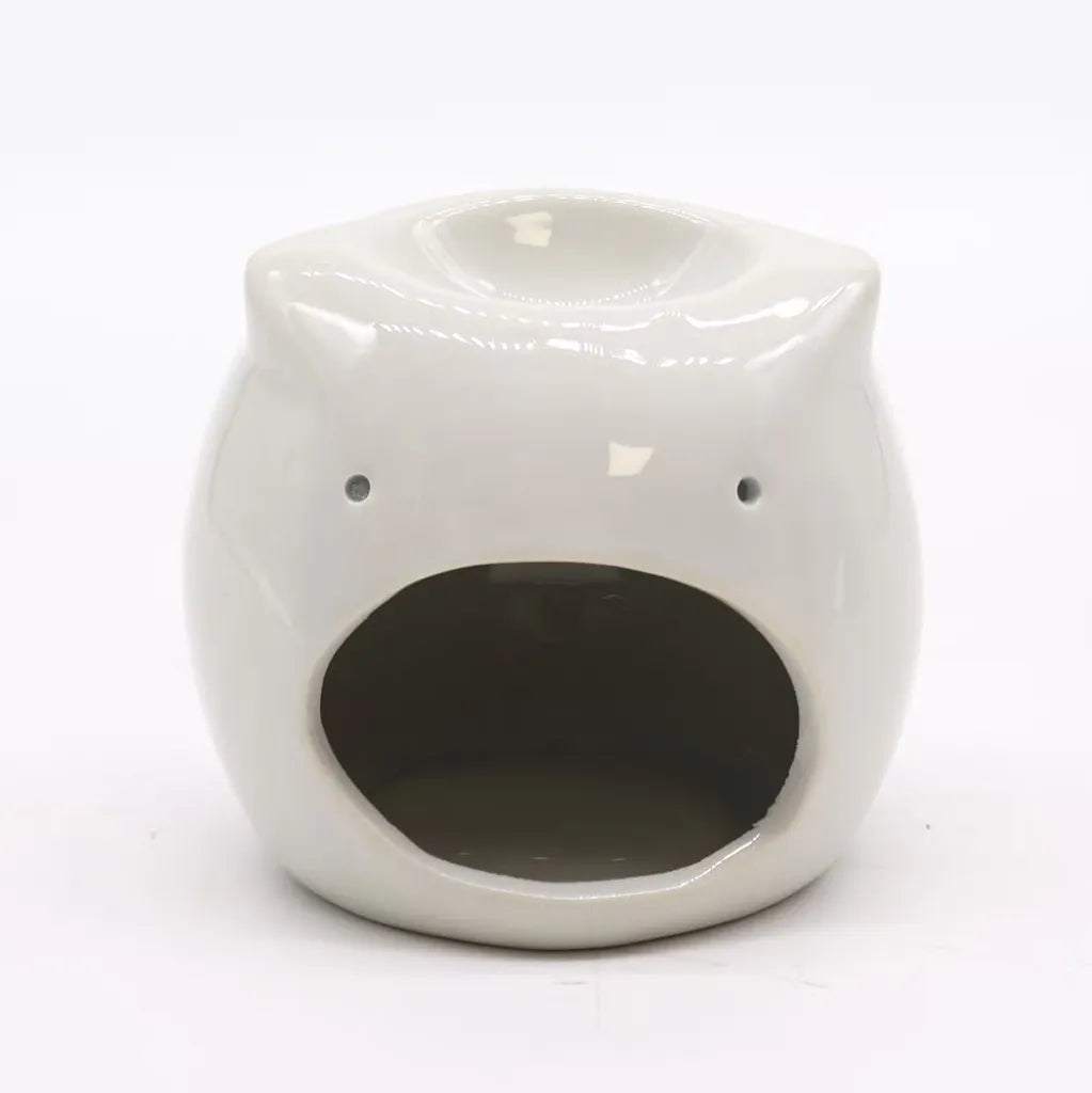 A white, glossy ceramic owl essential oil burner on a white background. The spherical owl has an open circular back for a candle, with a lit orange wax tea light inside. The top of the owl's head features a shallow dish for essential oils or wax melts.