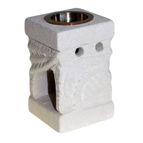 A square, cream-colored soapstone essential oil burner with an antique, carved design. The top of the burner features a brass bowl for essential oils or wax melts. The base has a wide, arched opening for a tea light candle and two small ventilation holes above it. The soapstone is detailed with carved abstract patterns on its sides, giving it a unique, artisanal look. The product is photographed against a clean white background, highlighting its rustic and handcrafted feel.