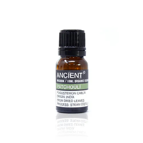 A small, 10ml amber glass bottle of Ancient Wisdom Organic Patchouli essential oil. The bottle has a black cap and a black label with a light green band. The label lists product details including the Latin name, origin, and distillation process. The bottle is photographed against a clean white background.