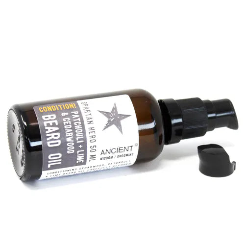 An amber glass bottle of Ancient Wisdom Spartan Hero Beard Oil, shown lying on its side on a white background. The bottle's black pump dispenser is visible, and the separate cap is placed nearby. The label is visible, detailing the "Patchouli, Lime & Cedarwood" scent.