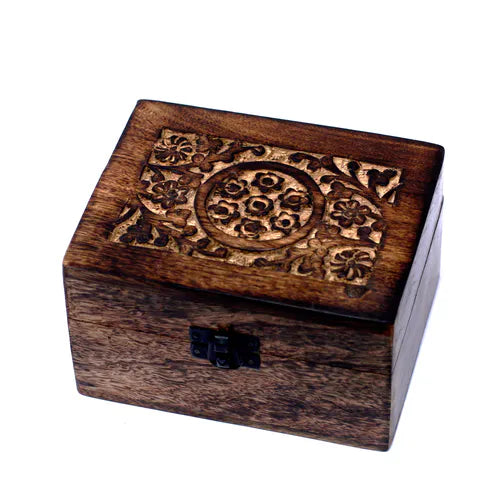 A small, square wooden box with a dark finish. The lid features an intricately carved floral pattern, including a central circular design surrounded by stylized flowers and leaves. A small black metal clasp secures the front of the box, which is photographed on a clean white background.