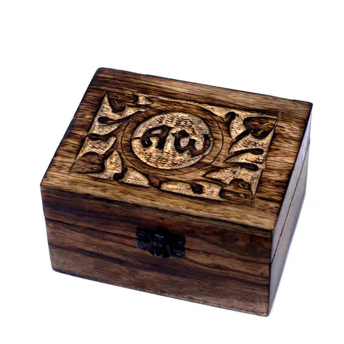 A small, square wooden box with a dark finish. The lid features an intricately carved spiritual pattern with the "AW" symbol in a central circular medallion, surrounded by stylized flowers and leaves. A small black metal clasp is on the front, and the product is photographed on a white background.
