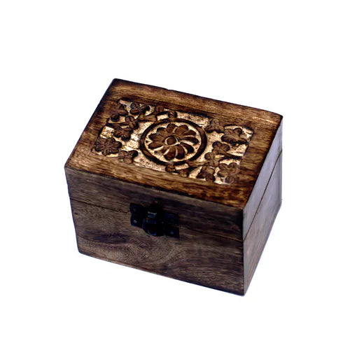 A small, square wooden box with a dark finish. The lid features an intricately carved floral pattern, including a central circular design surrounded by stylized flowers and leaves. A small black metal clasp secures the front of the box, which is photographed on a clean white background.