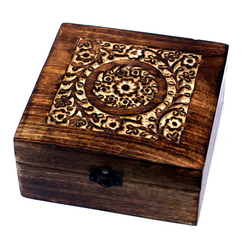 square wooden box with a dark finish. The lid features an intricately carved floral pattern, including a central circular design surrounded by stylized flowers and leaves. A small black metal clasp secures the front of the box, which is photographed on a clean white background.